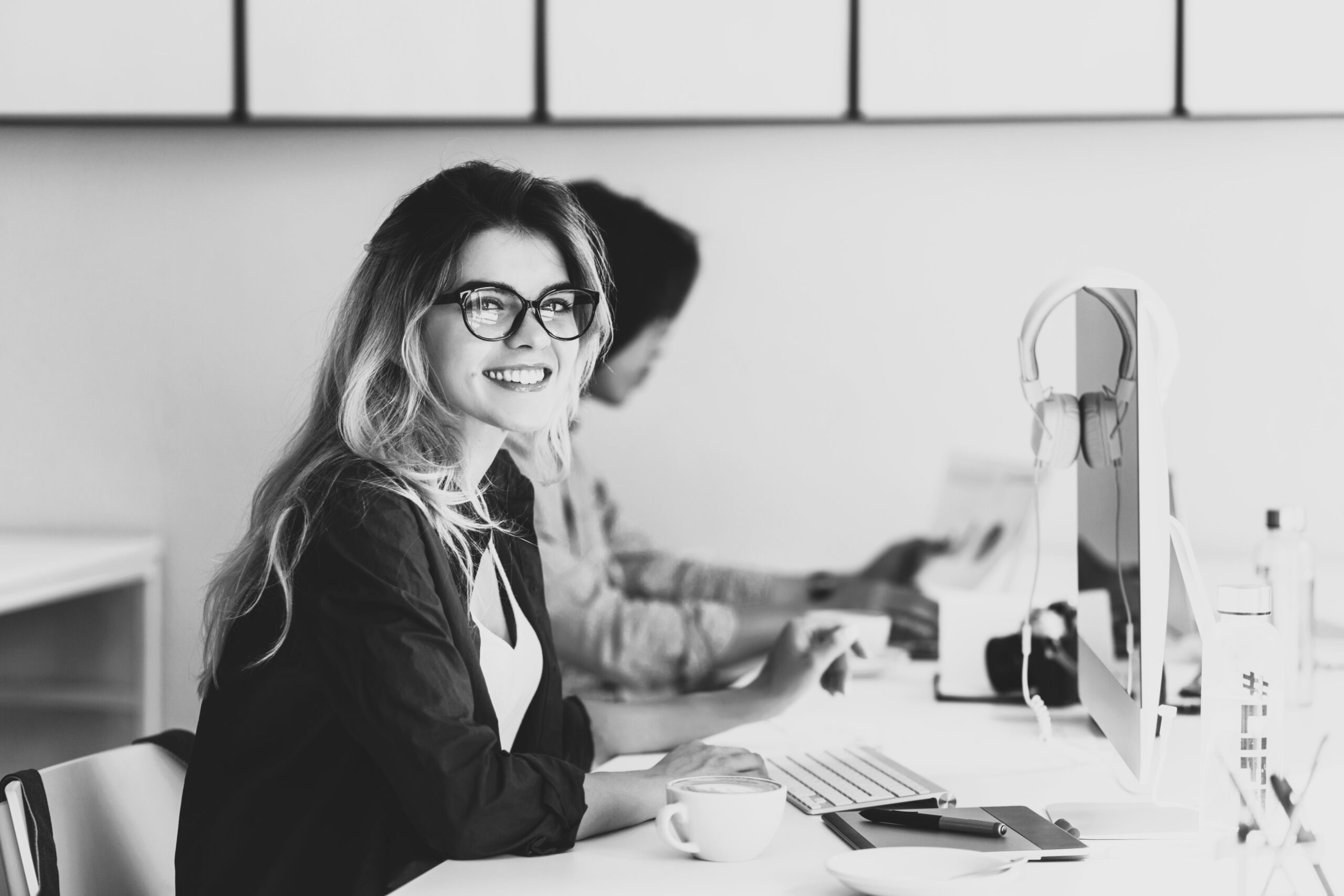 Attractive laughing freelancer girl posing with cup of coffee at her workplace. Chinese student in blue shirt works with document in campus with blonde friend in glasses.